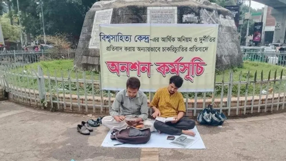 ঢাকা বিশ্ববিদ্যালয়ের রাজু ভাস্কর্যের পাদদেশে অনশনরত বিশ্বসাহিত্য কেন্দ্রের দুই কর্মকর্তা। ছবি: নিজস্ব